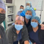 Diverse medical team wearing masks and scrubs smiles together in a clinic setting.